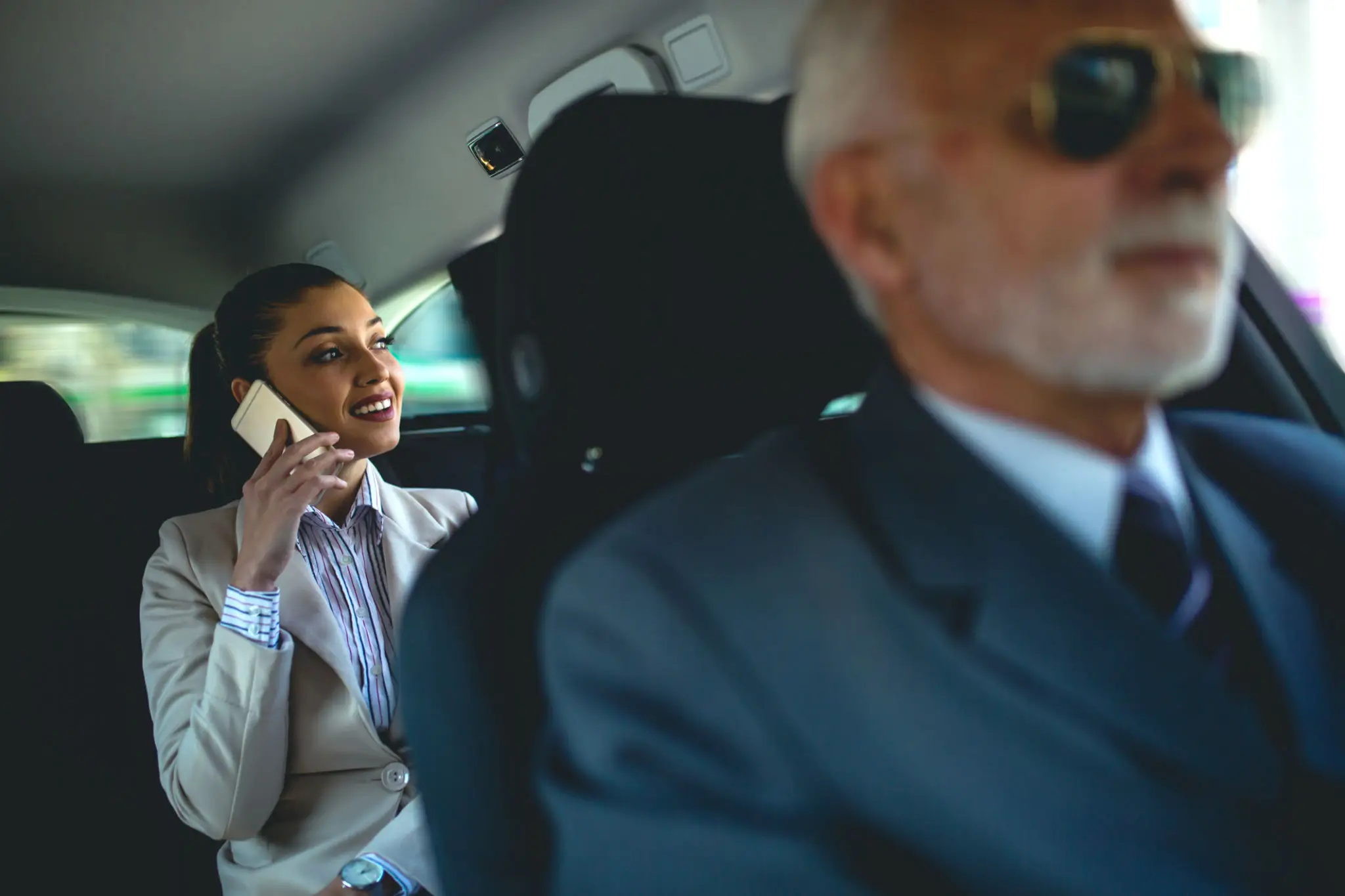 1e755cb6-6bc4-4d47-a241-8c35985857c2 A woman talking on her phone in a car with a driver.